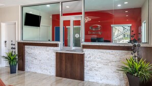 A reception area with a red wall, a glass door, and a digital display. - Econo Lodge Houston Northwest - Cypress (Houston)