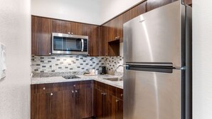 A modern kitchen with wooden cabinets, a stainless steel refrigerator, a built-in microwave, and a tiled backsplash. - Econo Lodge Houston Northwest - Cypress (Houston)