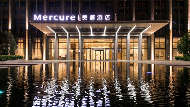 A hotel entrance with a reflective pool in front, a modern facade, and illuminated signage. - Mercure Xian Qujiang (Xi'an)