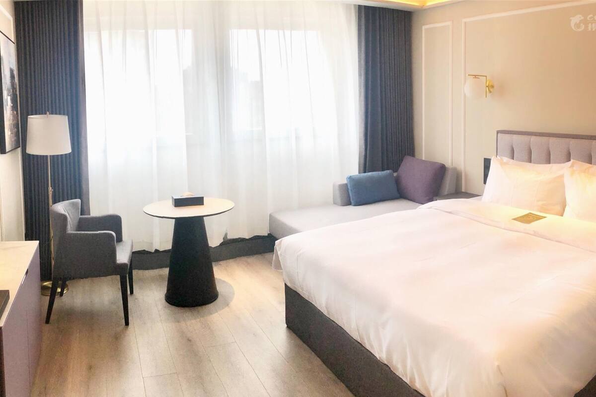 A hotel room with a large bed, a small table, a chair, and a sofa.