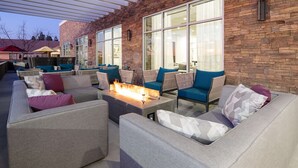 An outdoor seating area with sofas and chairs, a fire feature, and large windows. - Hyatt Place Bakersfield (Bakersfield)
