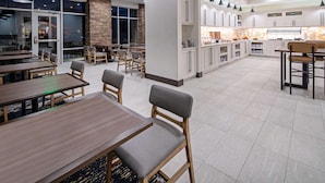 A modern restaurant with wooden tables and chairs, a stone accent wall, and a kitchen area with white cabinets and pendant lighting. - Hyatt Place Bakersfield (Bakersfield)