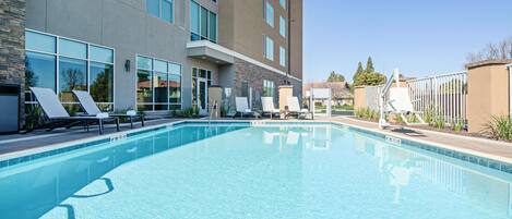 A swimming pool with lounge chairs and a building with large windows.