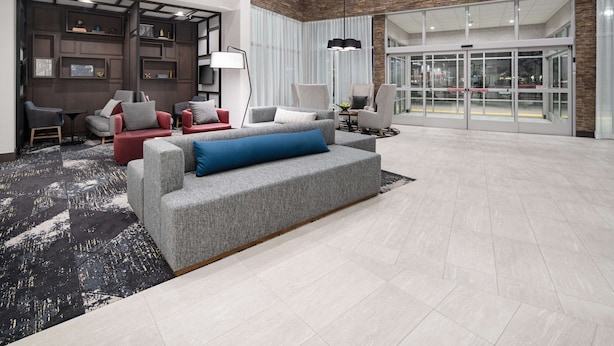 A spacious lobby with a grey sofa, red armchair, and a blue accent chair. There are wall-mounted shelves with decorative items and a large floor lamp. - Hyatt Place Bakersfield (Bakersfield)