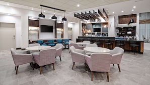 A modern hotel lobby with round tables and cushioned chairs, a bar area, and a flat-screen TV mounted on the wall. - Hyatt Place Bakersfield (Bakersfield)