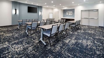 Un salón de conferencias con una mesa grande y sillas, una pizarra, un televisor de pantalla plana y una puerta con un letrero.