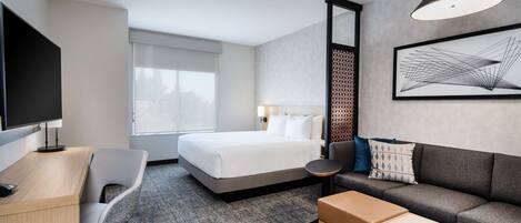 A modern hotel room with a bed, a desk, a chair, a sofa, and a coffee table.