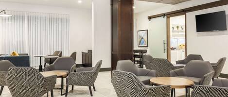 A modern lounge area with patterned chairs, a wooden table, and a TV mounted on the wall.