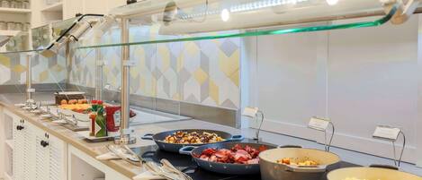 Zona de buffet con diversas opciones de comida, como ensaladas, carnes y cereales, dispuestas en un mostrador con mampara de vidrio.