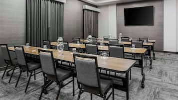 A conference room with a long table, chairs, a projector screen, and a large window with curtains.