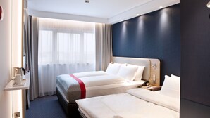 A hotel room with two beds, a desk with a lamp, and a window with curtains.