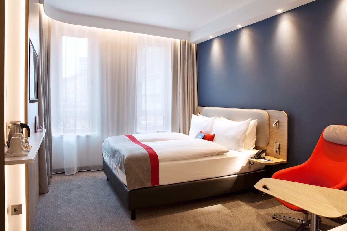 Une chambre d’hôtel avec un grand lit, un bureau avec une chaise et une fenêtre avec des rideaux.