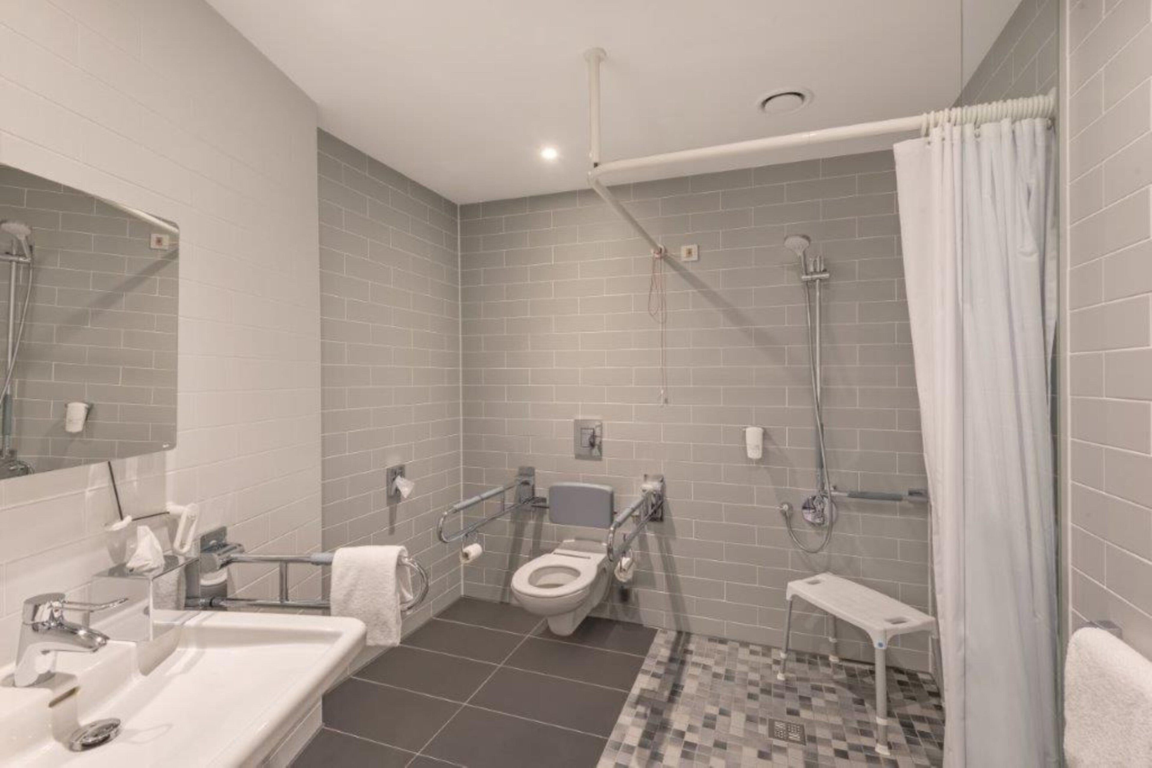 A modern bathroom with a toilet, sink, shower, and a small bench.