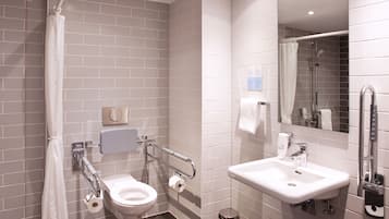 Un baño moderno con inodoro, lavamanos y ducha. Presenta azulejos blancos, un pasamanos y un espejo.