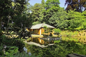 A traditional Japanese-style house with a tiled roof, surrounded by lush greenery and a calm pond.