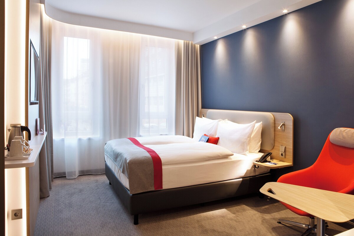 Een hotelkamer met een bed, een bureau, een stoel en een raam met gordijnen.
