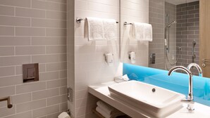 A modern bathroom with a white sink, a glass shower enclosure, and a blue accent wall.