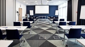 Une salle de conférence dotée d’un tapis à motifs géométriques, de tables blanches et de chaises bleues.