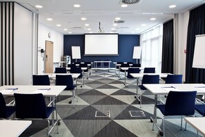 A conference room with a geometric patterned carpet, white tables, and blue chairs.