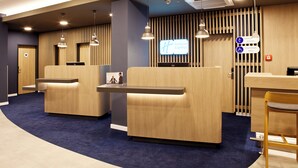 Un espace d’accueil comprenant un comptoir, deux coins salon et un panneau indiquant l’emplacement de l’hôtel Holiday Inn Express.