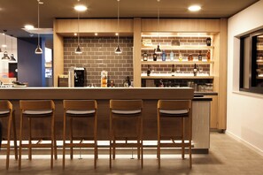 A modern bar area with wooden bar stools, a brick wall, and shelves with bottles. - Holiday Inn Express Kaiserslautern by IHG (Kaiserslautern)
