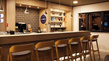 A bar area with wooden chairs, a counter with a tap, and shelves with bottles.