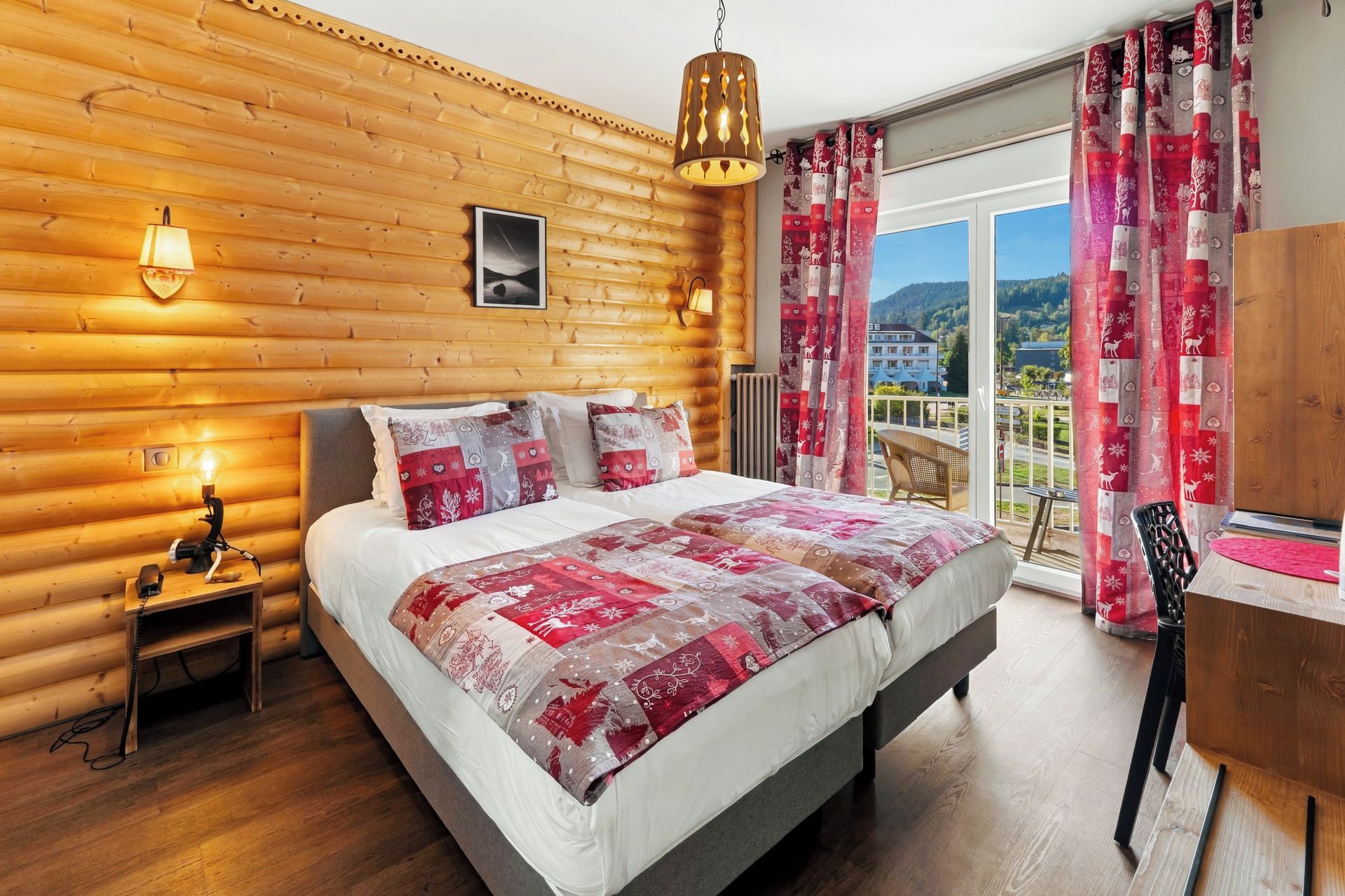 A log cabin-style bedroom with a bed, bedside lamps, a view of the outside, and a balcony with a chair.