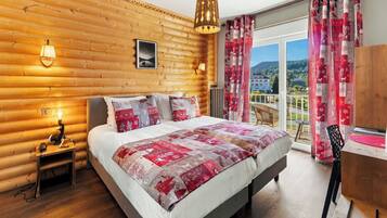 A log cabin-style bedroom with a bed, bedside lamps, a view of the outside, and a balcony with a chair.