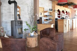 A cozy interior with a wood-burning stove, leather chairs, and a wine display. - L’Annexe by La Réserve (Gerardmer)