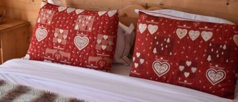 Une chambre dans un chalet en bois, avec un lit, deux oreillers ornés de motifs en forme de cœur et une couverture moelleuse.