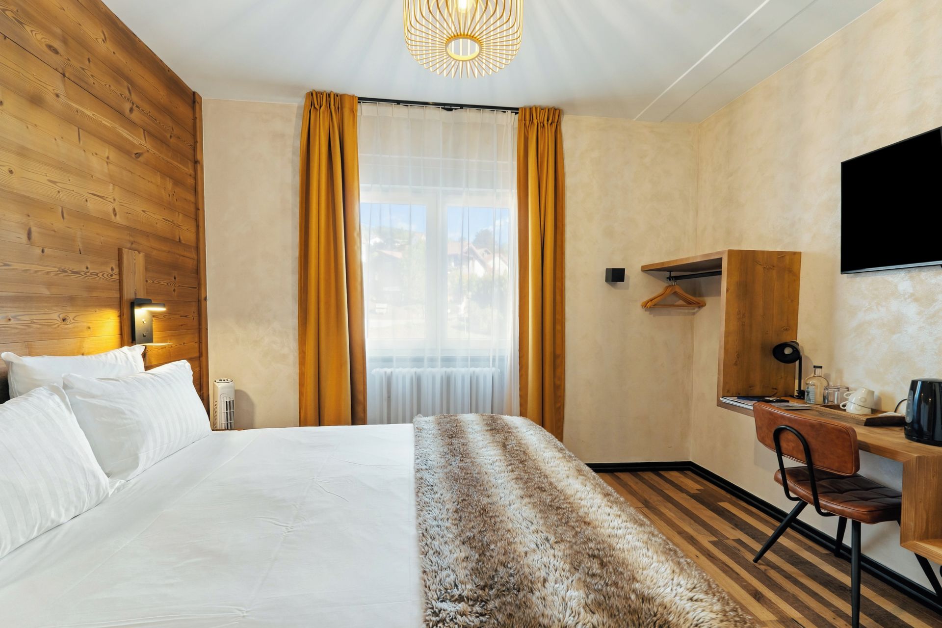 Habitación de hotel con una cama grande, un escritorio, una silla, un televisor y una ventana con cortinas.