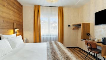 Habitación de hotel con una cama grande, un escritorio, una silla, un televisor y una ventana con cortinas.