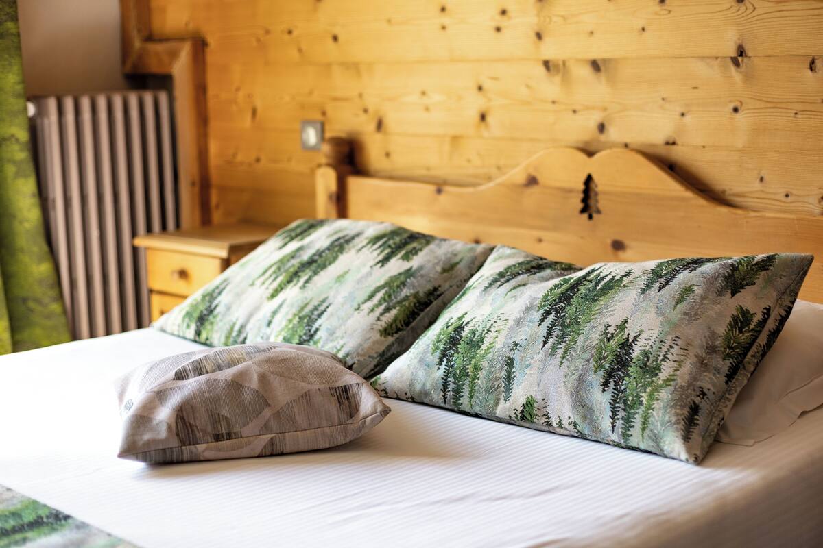 A bed with two pillows, one with a leaf pattern and another plain.