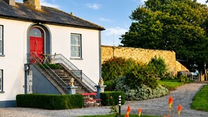A white building with a red door, a staircase, and a stone wall in the background. - Nore View House (Dunbell)