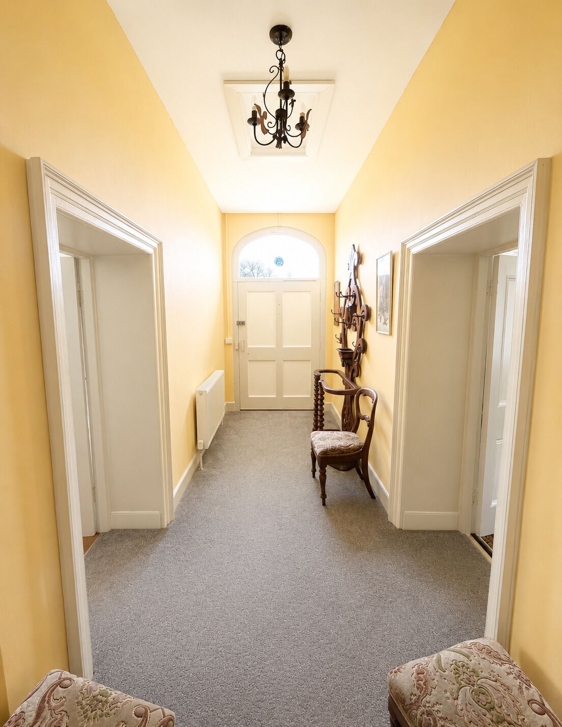 A hallway with a chandelier, a chair, and a radiator.