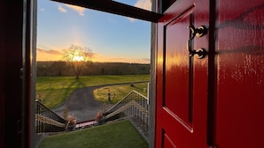 A red door with a view of a sunset over a grassy field and a tree. - Nore View House (Dunbell)