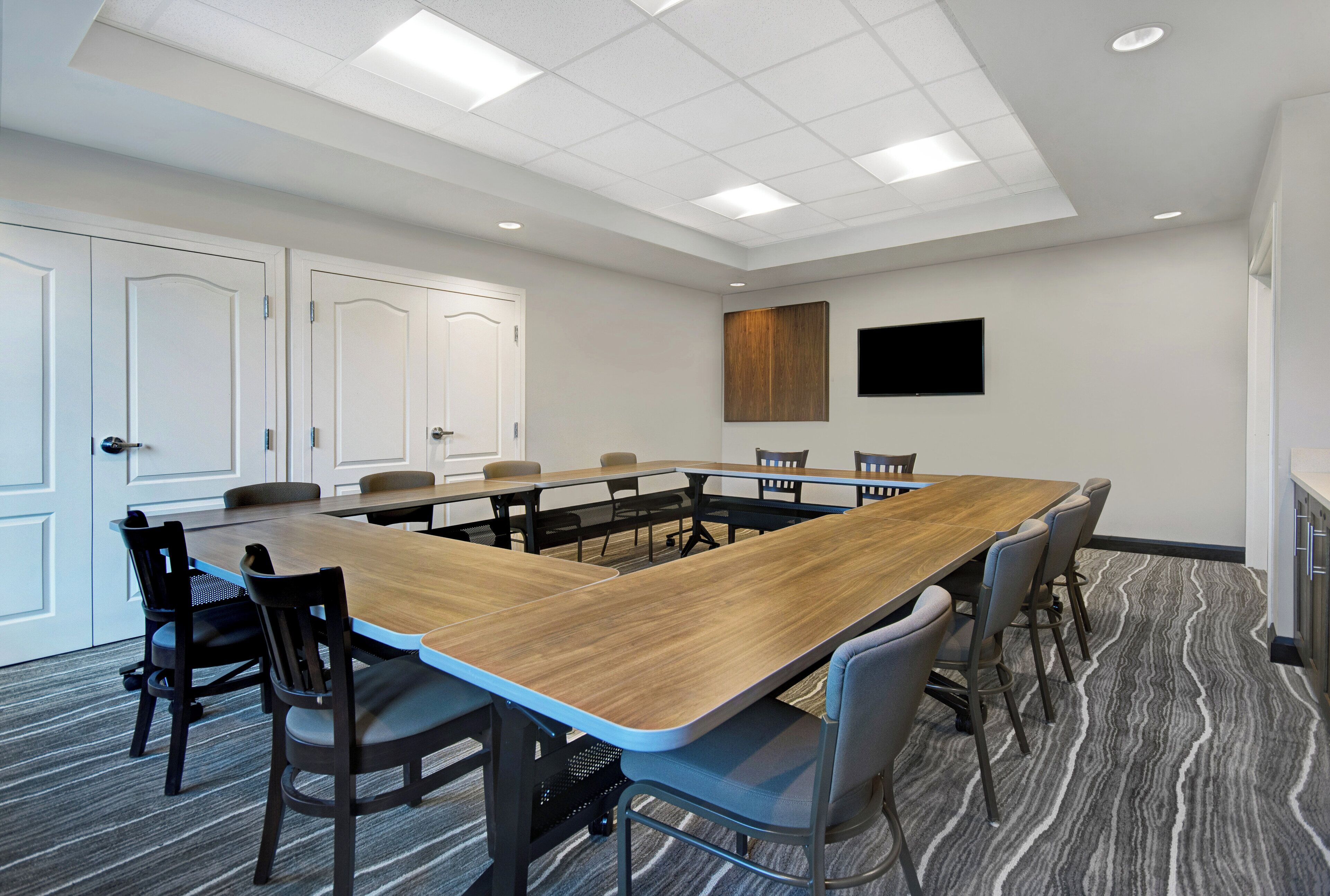 A conference room with a long table, chairs, a flat-screen TV, and a door.