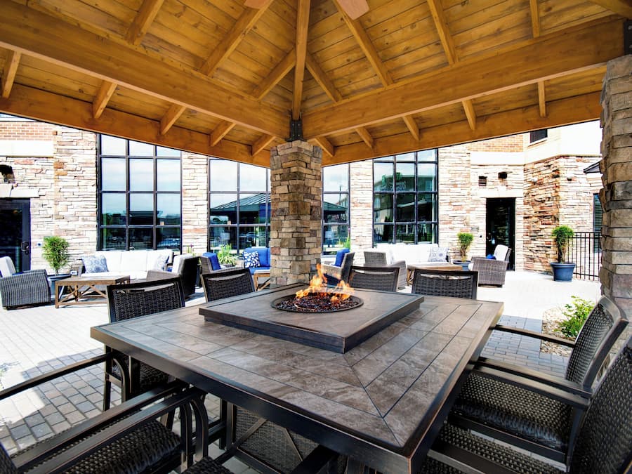 An outdoor patio area with a stone fireplace, seating arrangements, and a view of the surrounding buildings.