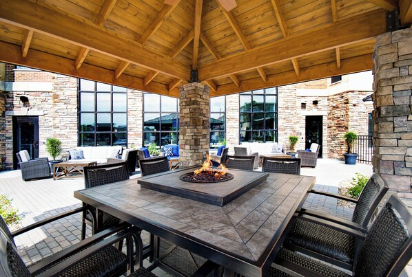 An outdoor patio area with a stone fireplace, seating arrangements, and a view of the surrounding buildings. - Staybridge Suites Sterling Heights - Detroit by IHG (Sterling Heights)