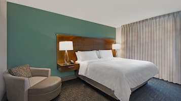 Habitación de hotel con una cama grande, una silla, una mesita de noche y un ventanal con cortinas.