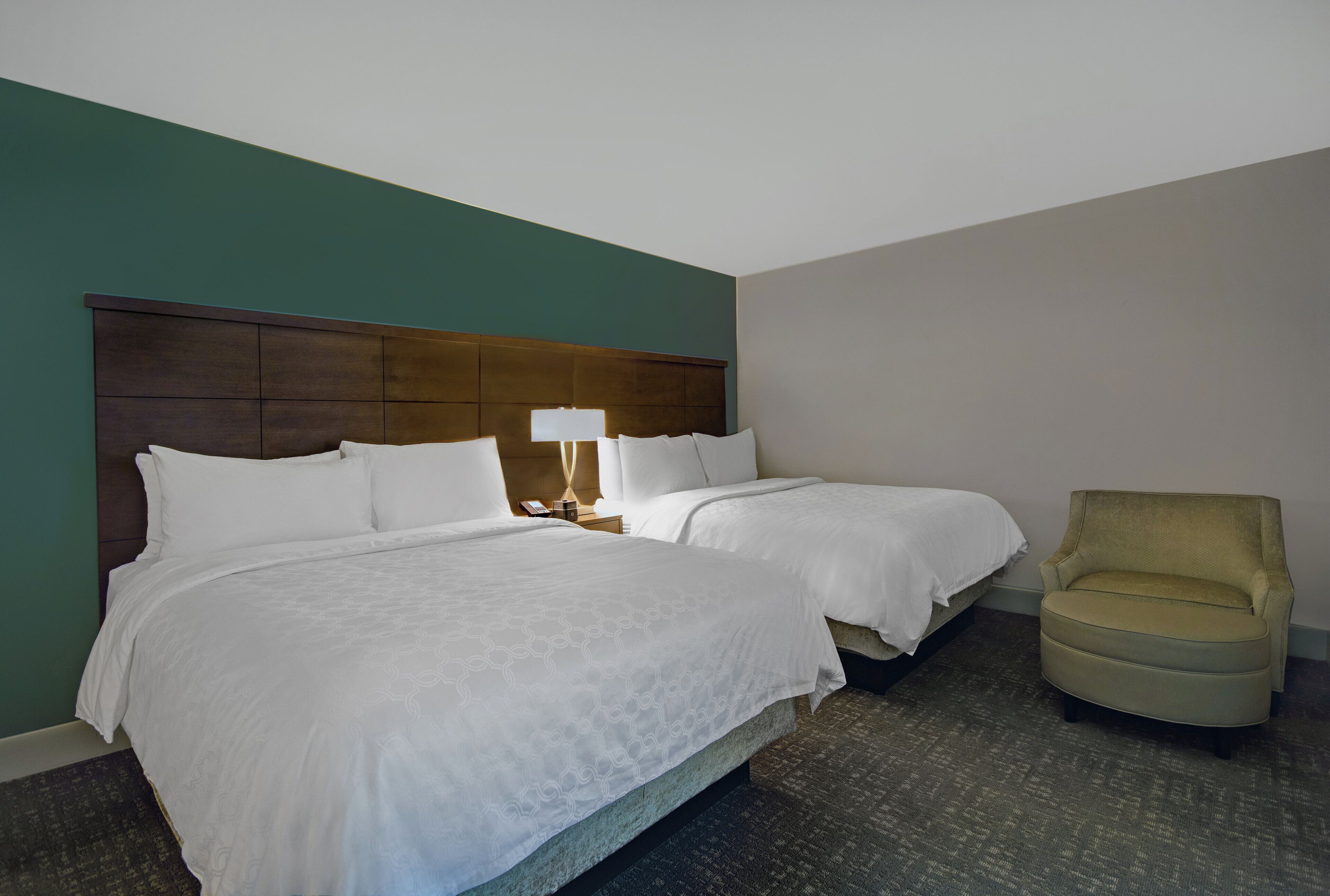 A hotel room with two beds, a nightstand, a lamp, and a chair.