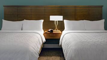 A hotel room with two beds, a nightstand with a lamp, and a wooden headboard.