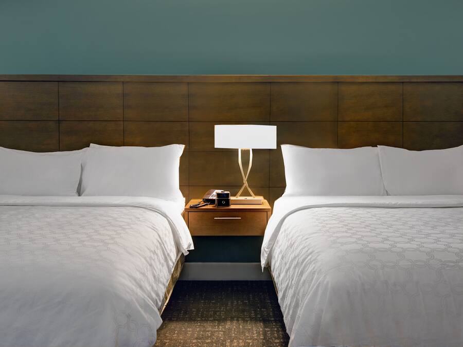 A hotel room with two beds, a nightstand with a lamp, and a wooden headboard.