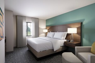 Habitación de hotel con cama, lámparas de noche, mesita de noche, una silla y vista al exterior.