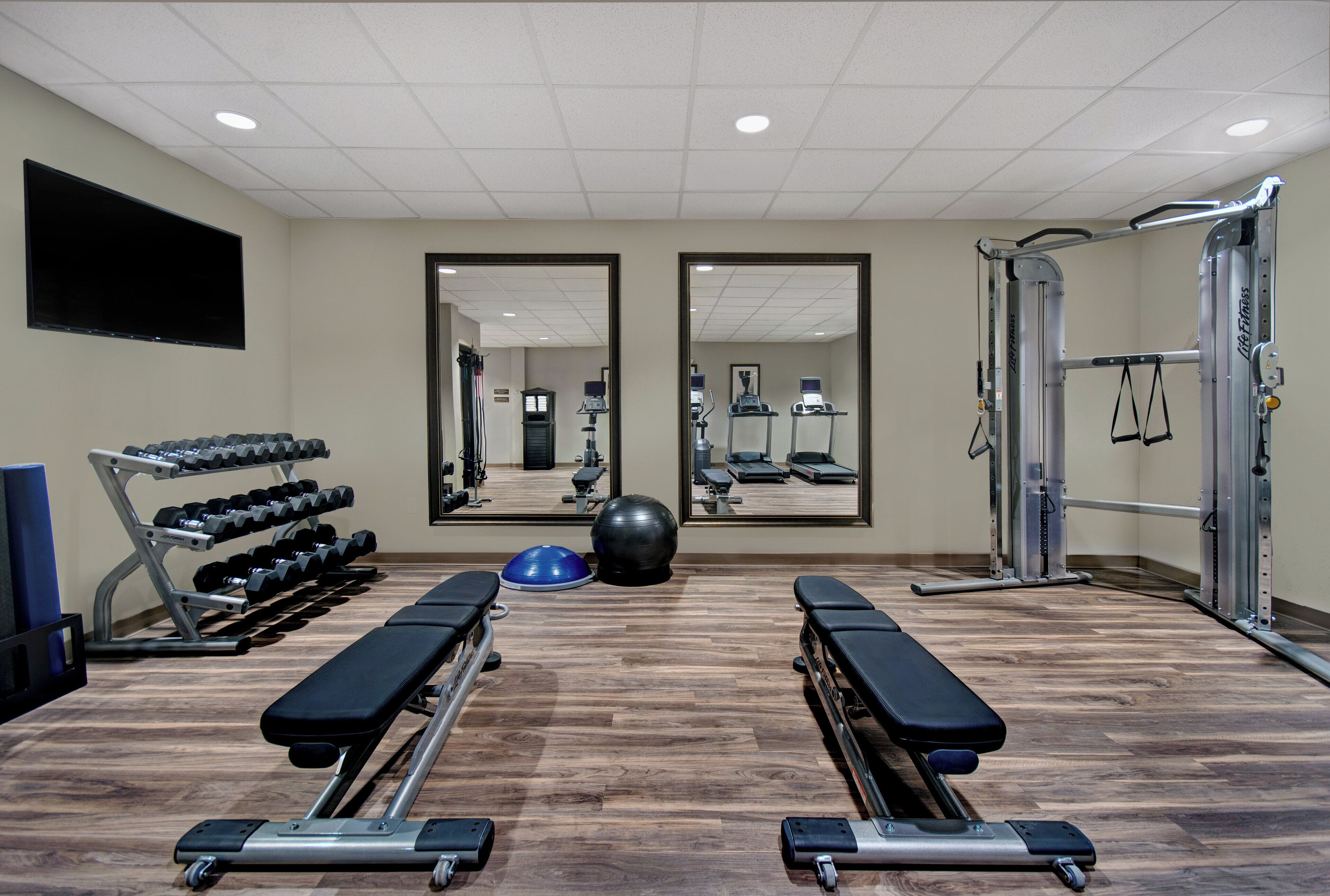 A gym with exercise equipment, benches, a mirrored wall, and a television.