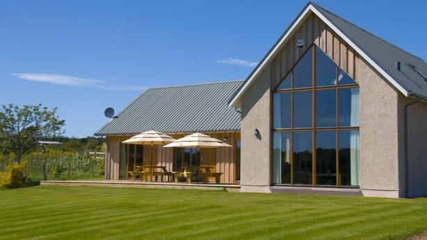 A modern house with a large glass window, a covered patio with outdoor furniture, and a well-maintained lawn.