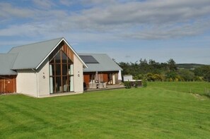 A modern house with a large glass window, a covered patio, and a well-maintained lawn.