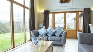A spacious living room with a large window, a grey sofa, and a wooden coffee table with glasses.