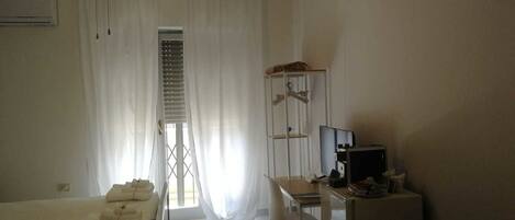 A bedroom with a bed, a desk, a chair, a ceiling fan, and a window with curtains.