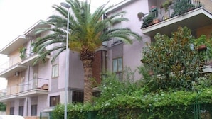 A multi-story residential building with balconies, a palm tree, and a green fence. - Gatto Bianco Picone 19 (Bari)